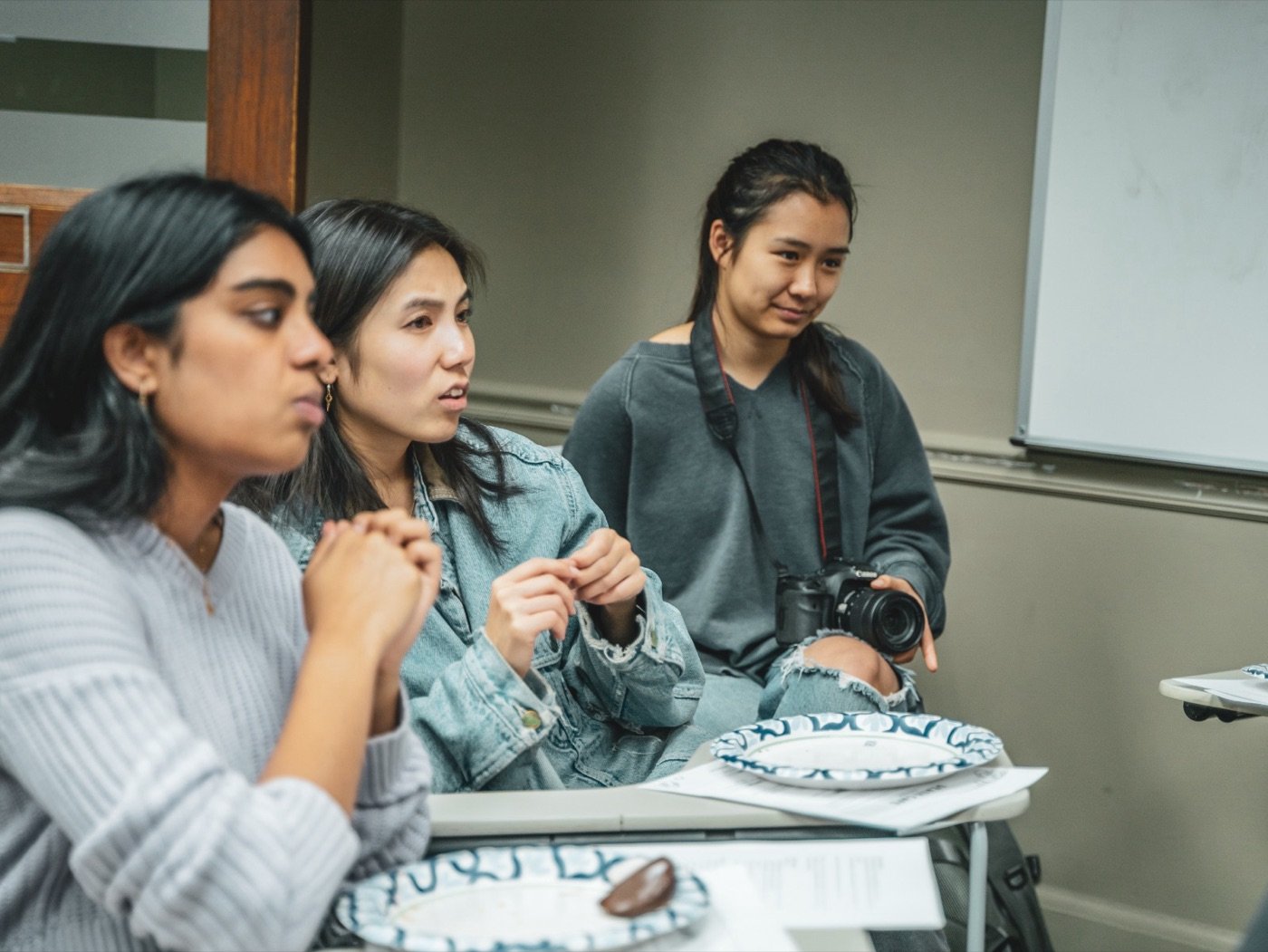 Three students in conversation, one holding a camera